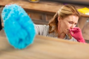 Woman Coughing While Dusting A Dirty Shelf